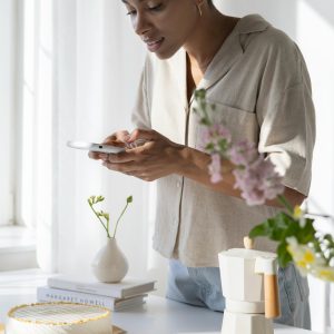 Woman Capturing A Stylish Coffee Setup In A Sunlit Kitchen With Flowers And Cake.