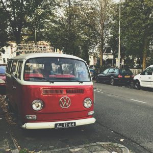 A Vintage Red Volkswagen Combi Van Parked On A Tree Lined Street In A City Environment.