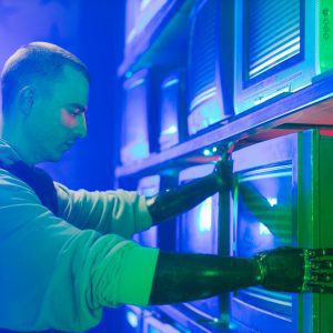 Man With Prosthetic Arms Interacting With Stack Of CRT Televisions, Showcasing Technology.
