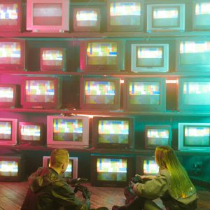 Cyberpunk Aesthetic With Neon Lights And Vintage TVs. Two People Absorbed In Retro Tech.