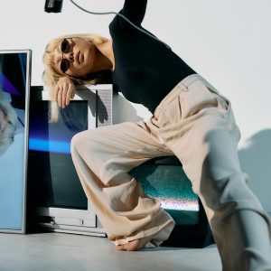 Chic Editorial Fashion Shoot Featuring A Stylish Model Interacting With Electronics And Posing Creatively.