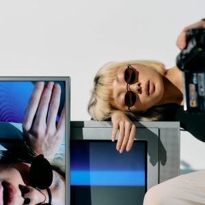 Stylish Portrait Featuring A Fashion Model With CRT Monitors And A Vintage Camera.