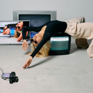 A Stylish Fashion Model Poses In A Studio With Vintage TV Sets, Creating An Edgy And Trendy Scene.