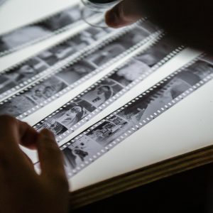 Close Up Of Hands Examining Vintage Film Strips On A Light Table, Evoking Nostalgia.