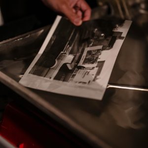A Close Up Of A Hand Developing Black And White Photographs In A Darkroom With Vintage Processing Equipment.