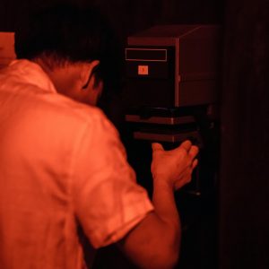 Photographer Working In A Darkroom Under Red Lighting To Develop Film Using Analogue Technology.