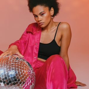 Fashionable Woman In Vibrant Attire Posing With A Disco Ball In A Studio.