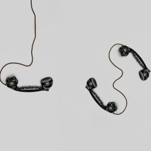 Two Vintage Black Telephone Handsets Connected By Cords On Gray Background.