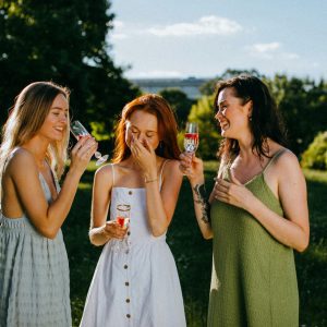 Three Women Enjoying A Sunny Day With Drinks, Celebrating Friendship Outdoors.