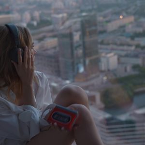 Caucasian Woman Listening To Music On A Cassette Player By A High Rise Window At Dusk.