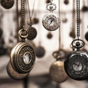 Close Up Of Antique Pocket Watches With Intricate Designs Hanging In A Blurred Vintage Setting.