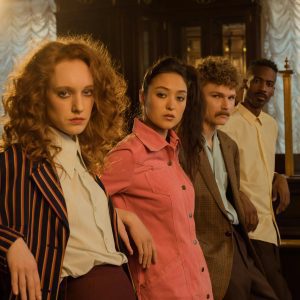 Diverse Group Of Adults Posing In Stylish Retro Attire Indoors With A Serious Expression.
