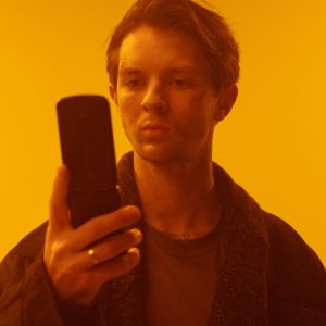 Portrait Of Man With A Flip Phone In A Warm, Cyberpunk Themed Room.