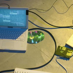 An Overhead View Of A Vintage Electronics Setup Featuring A Laptop And Disks With Tangled Cables.