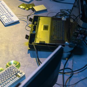 Cyberpunk Themed Setup With Laptops, Keyboards, Wires, And Retro Tech Items In A Dim Room.