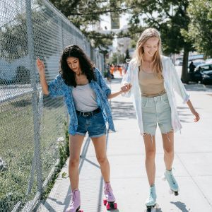 Two Teenagers Roller Skate On A Sunny Day, Enjoying Togetherness And Fun.