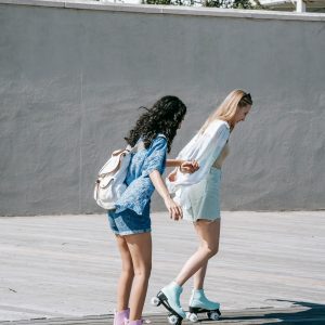Two Women Roller Skate Outdoors On A Sunny Day, Having Fun And Enjoying Each Other's Company.