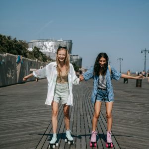 Two Young Women Roller Skating On A Sunny Day, Enjoying Their Leisure Time Together.