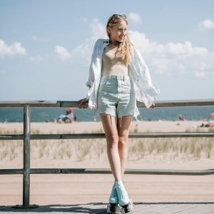 Smiling Young Woman Enjoying A Sunny Day Roller Skating By The Beach With A Scenic Ocean View.