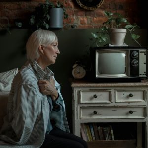 Serene Elderly Woman Wrapped In Blanket Beside Vintage TV, Evoking Nostalgia And Warmth.