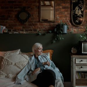 Elderly Woman Relaxing In A Rustic Bedroom With Vintage Decor And Warm Lighting.