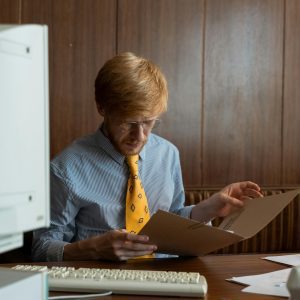 Vintage Office Scene With A Man Reviewing Documents On An Old Computer Desk.