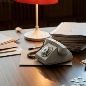 Retro Desk Setup With Rotary Phone, Red Lamp, And Documents Suggesting A Classic Office Vibe.