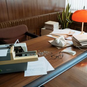 A Retro Office Desk Featuring A Typewriter, Vintage Telephone, And Stacks Of Documents.