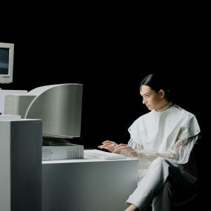 A Stylish Woman Works On A Vintage Computer In A Minimalist, Studio Setting.