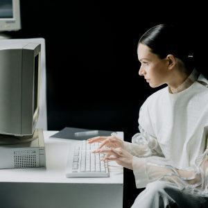 A Woman In Modern Attire Using A Vintage Computer In A Dark Setting, Blending Past And Future.