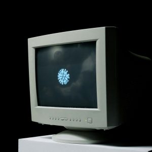 A Vintage Computer Monitor Shows An Image Of A Coronavirus On Screen Against A Dark Background.