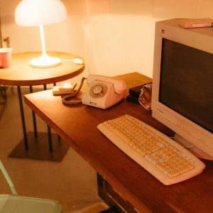 A Cozy, Vintage Workspace Featuring A Rotary Phone, CRT Monitor, And Warm Lamp Lighting.