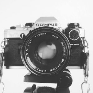 Black And White Image Of A Classic Olympus Camera With A 50mm Lens In Focus.