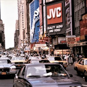 A Bustling Scene Of Vintage Cars And Iconic Billboards In Times Square.
