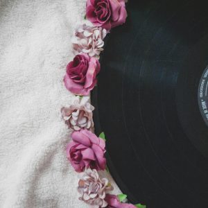 A Vintage Vinyl Record Decorated With Vibrant Pink And Purple Roses On A Textured Fabric Background.