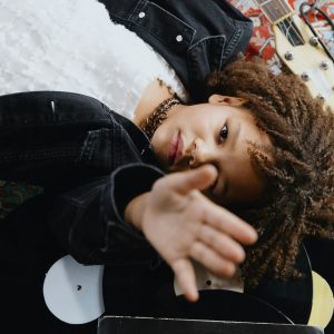 A Child Lying Down With A Guitar And Vinyl Records In An Artistic Composition Indoors.