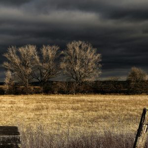 Scenic View Of A Countryside Field With Dark Storm Clouds Overhead, Capturing A Moody And Dramatic Atmosphere.