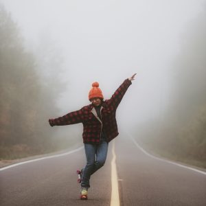 A Woman In A Plaid Jacket And Beanie Skates On A Foggy Rural Road, Embracing Freedom And Adventure.