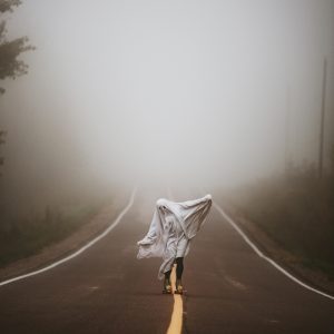 Mysterious Person Skating On Foggy Road, Draped In A Ghostly Costume, Perfect For Halloween Themes.