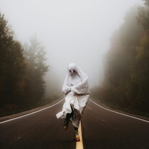 Foggy Road With A Person In A Ghost Costume Roller Skating. Eerie And Playful Atmosphere.
