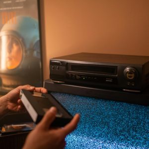 Person Inserting VHS Tape Into Video Recorder With Static TV In Cozy Room.