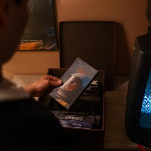 A Person Examining Vintage VHS Tapes In A Cozy Indoor Setting With A Retro TV.