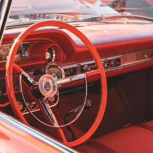 Classic Red Car Interior Featuring A Vintage Steering Wheel And Dashboard Design.