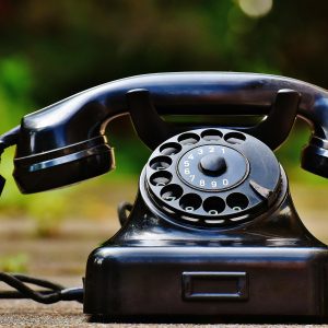 Close Up Of A Classic Black Rotary Phone Outdoors With A Blurred Green Background.